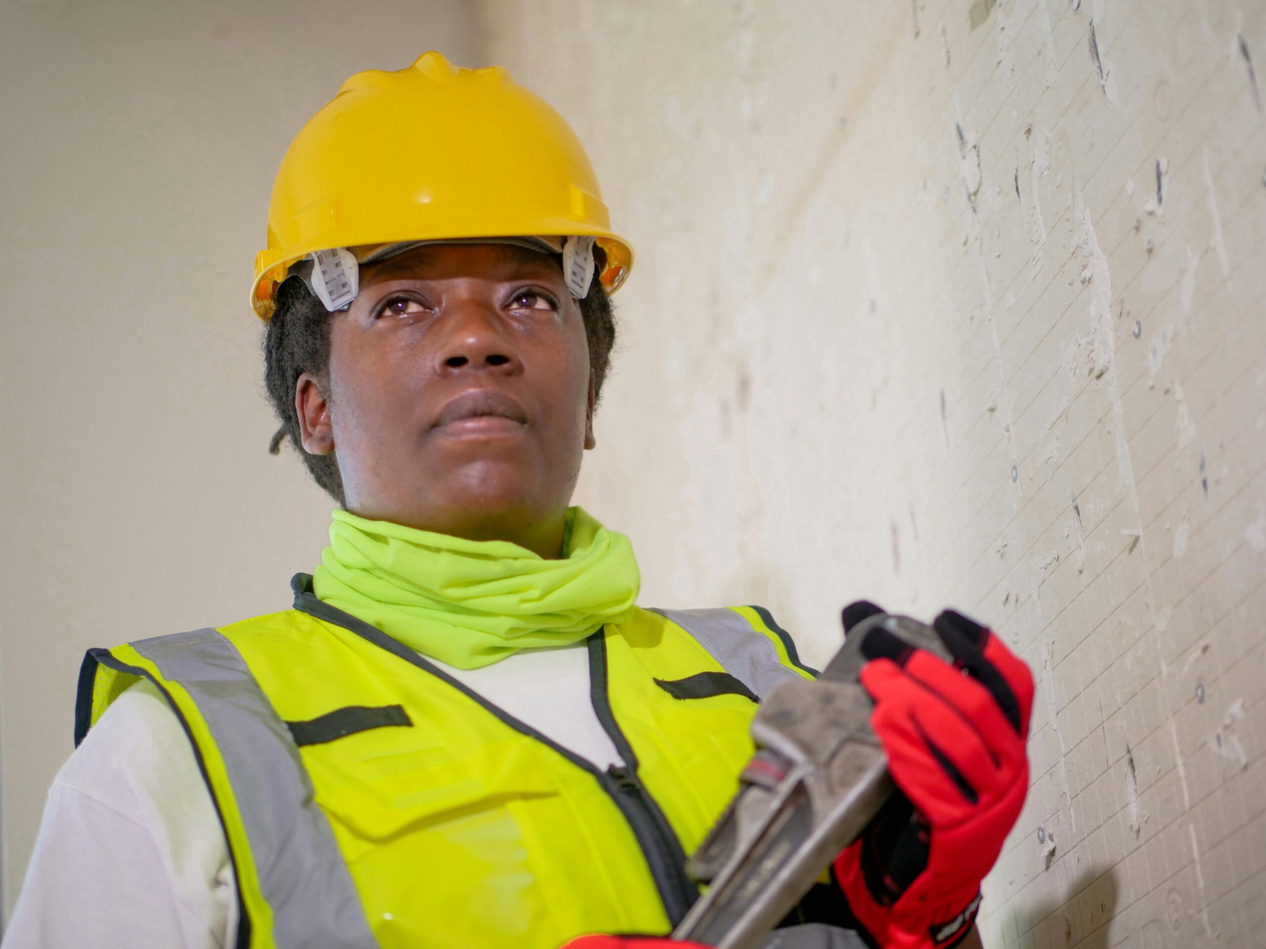 Portrait of a female construction worker in safety gear holding a wrench indoors.